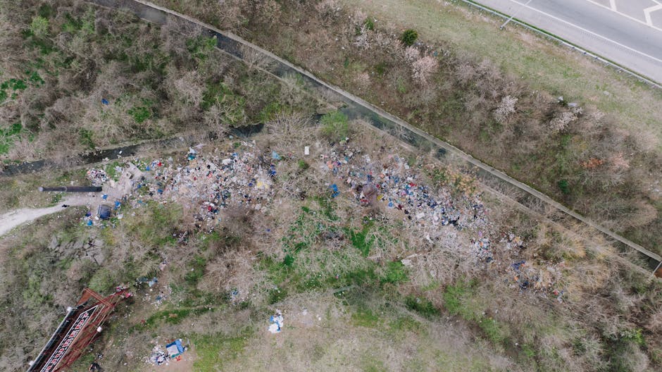 A large open area of ground covered with a significant accumulation of mixed waste materials, primarily plastic and paper rubbish, forming a dense heap stretching across the foreground. The plastic wa